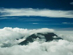 White cloud surrounds and caps dark mountaintop with blue infinity sky behind.  Mount Merapi, Indonesia Stock Footage