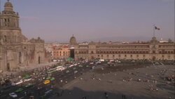 Traffic drives by historic buildings and a billowing Mexican flag in the Zocalo of Mexico City. Stock Footage