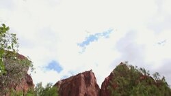 Tilt down from blue skies to young boy with outstretched arms with rocky mountains behind him Stock Footage