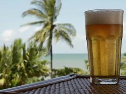 MS Lockdown of a glass of cold beer on a table and a beach in the background Stock Footage
