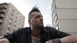 Cool young man with mohawk smoking electronic cigarette below urban buildings Stock Footage