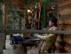 Cowboy sits on porch outside log cabin Stock Footage