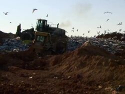 Medium zoom-out - Bulldozers drive over a landfill where seagulls scavenge Stock Footage