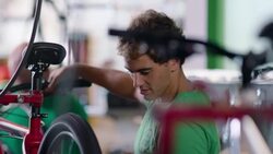 Mechanic adjusts levers on bicycle handlebar and inspects spinning wheel in busy bike shop Stock Footage