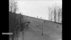 1950: WINTER SNOW SKIING: Two skiers moving down hill in powder snow. WS Ski slope. Couple dressed in warm clothing talking on slope. Pair of snow skiers moving down bumpy hillside, one falling down.  Winter sports. Instructional Video