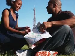 couple looking at a map while sitting on the grass in front of the Eiffel tower Stock Footage