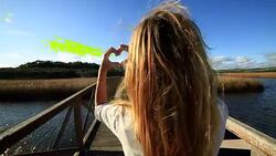 Woman makes heart shape finger frame on bridge above lake Stock Footage