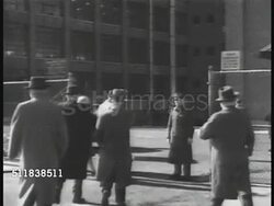1941: US INDUSTRY: WS People in coats walking through guarded gate, security guard checking worker's lapel button. WS Lockheed Aircraft factory w/ unfinished plane being moved off tarmac. WS Workers guiding unfinished aircraft, riveters riveting. Instructional Video