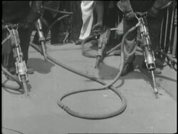 Construction workers use jackhammers to break up pavement and dump the rubble into a truck. News Clip