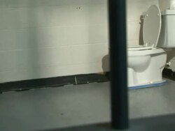 Medium hand-held tracking-right - A jail cell features a cot and a toilet. / USA Stock Footage