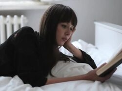 CU TD Young woman on bed reading book by open window / Berlin, Germany Stock Footage