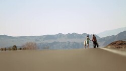 Couple walk up a desert road in the sweltering heat, young man points out something in the distance Stock Footage
