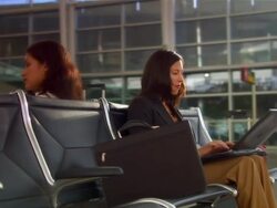 Dolly around woman working on laptop while waiting for flight at airport to woman on seat behind her talking on cell phone Stock Footage