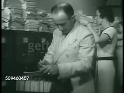 1938: US COAST GUARD INTELLIGENCE: File room w/ men walking between rows. CU File cabinet hand-written tags 'Sinking of 'I'm Alone' ', 'Vessels Suspected of Smuggling' CU Male hands holding Treasury Department Arrest Record cards w/ mug shots. Instructional Video