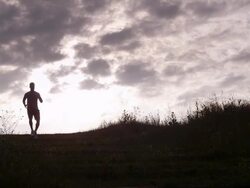 WS handheld silhouette male athlete running down hill  Stock Footage