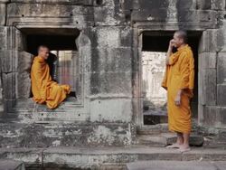 WS A Buddhist monk attempts to meditate while another talks and laughs on a mobile phone at an ancient temple in Angkor Wat / Siem Reap, Cambodia Stock Footage