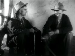 B/W 1936 man holding pump handle talking to other man carving wood / migrant workers Stock Footage