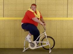 Medium shot fat man riding exercise bicycle and looking over shoulder Stock Footage