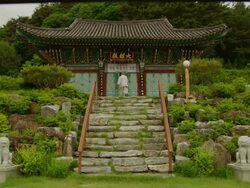 Wide Shot Locked Down - Old man climbs stairs to buddhist temple and opens its doors / South Korea Stock Footage