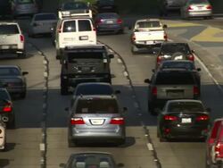 High Angle pan-right - A police officer stands with a group of travelers next to two vehicles on the median as traffic travels past. / Los Angeles, California, USA Stock Footage