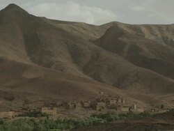 Mountains slump down to the valley below, revealing a small, rustic settlement. Stock Footage