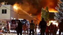 Bystanders watch from across the street as firefighters shoot water onto fire Stock Footage