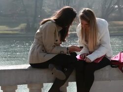 Teenage girls check text on marble rail, river below Stock Footage