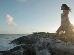 Young woman standing on rocks by the sea with breeze blowing her dress Stock Footage