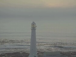 WS AERIAL PAN View of Lighthouse and ocean at sunset sunrise with lighthouse light turning round Stock Footage
