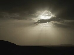 Clouds move over and surround angelic sunlight, as it shines down over a darkening landscape. Stock Footage