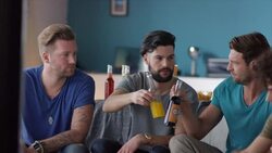 Guys sitting on couch watching tv and clinking bottles Stock Footage