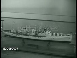 1938: DESIGNING VESSELS: Sign 'United States Coast Guard' INT Conference room w/ meeting in progress. Model of Coast Guard Cutter. VS Boat designers working, men looking at blueprints. Coast Guard Patrol Craft. Designers working on blueprint. Instructional Video