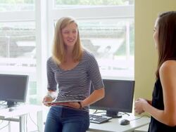 MS two female students leaning against desk in computer lab discussing project on digital tablet Stock Footage