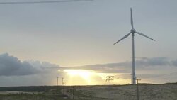 The sun shines through clouds over a wind turbine spinning on a hill. Stock Footage