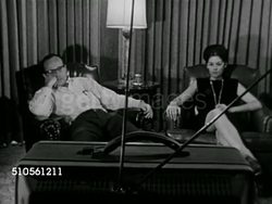 1965: WATCHING TELEVISION: WS Male & female sitting in chairs watching small TV w/ rabbit ears FG, man shifting forward in seat, MS (Beside) Male sitting forward in seat, female sitting w/ feet on ottoman BG, ZI MS Male. Instructional Video