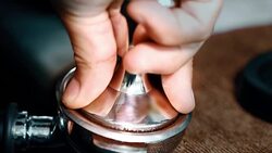 Barista using a tamper to press ground coffee into a portafilter Stock Footage
