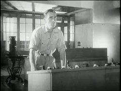 A man in a power plant stands behind a control panel turning knobs and adjusting gauges. News Clip