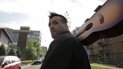 Cool young man walking carrying guitar over shoulder on sunny urban street Stock Footage