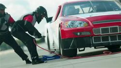 A pit crewman tightens the lug nuts on a stock car, and the car speeds away. Stock Footage