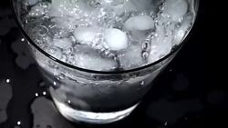 Pouring water into glass of ice with splashes at slow motion on black background Stock Footage