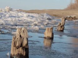 Dutch angle skewed tracking shot of a frozen lake, snow, ice, trees and pilings. - Model Released - 1920x1080 - HD Stock Footage