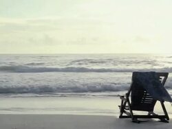 Deck chair on sandy beach at water's edge Stock Footage