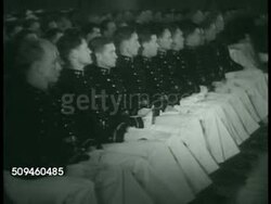 1938: US COAST GUARD ACADEMY: GRADUATION: MS Bugler (no SOT). WS Officers on stage. WS Cadets in uniforms sitting. CU USCG Academy diploma. CU Commission papers. Cadets walking on stage receiving diploma & Commission. MS Cadets applauding. Instructional Video