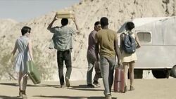Group of friends wander aimlessly in the desert, guy balances and tosses suitcase in the air Stock Footage
