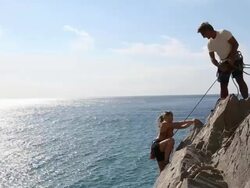 Father belays daughter on rock climb above sea Stock Footage