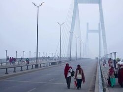 Morning travellers on foot cross long roadbridge on sidewalk, carrying possessions and wearing warm clothing.  India Stock Footage