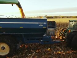 The auger from a combine finishes dumping corn into a wagon and it pulls away at sunrise. Stock Footage