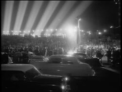 B/W 1956 wide shot PAN crowd, traffic + klieg light beams in front of Grauman's for Giant premiere / night Stock Footage