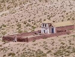 WS View of primitive stone church looking structure with flag blowing in wind thatched roof and white colored front walls in middle of light brown desert with small green shrubs Stock Footage