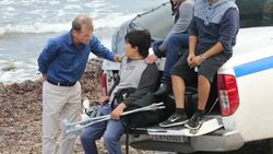 A disabled Syrian migrant who has fled the war and escaped to Europe, landing on the Greek island of Lesvos on the north coast at Efthalou, is helped by the Greek police. Up to 4,000 migrants a day are landing on the island and overwhelming the authorities Stock Footage